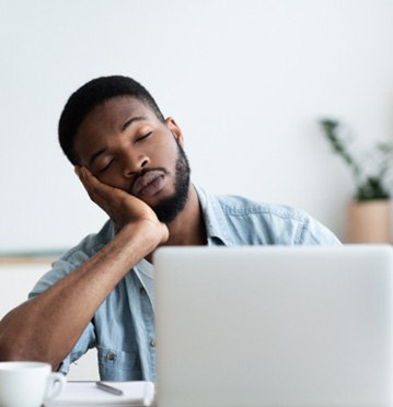 Man sitting at his desk in front of his laptop head in his hand asleep