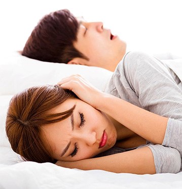 Woman covering ears while man snores before laser snoring treatment