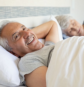 Older smiling man and woman lying in bed after laser snoring treatment Albuquerque, NM