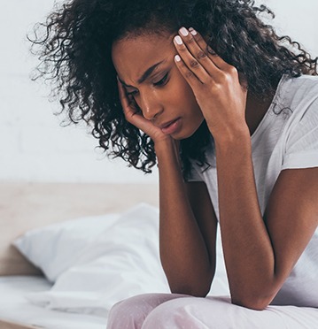 Woman sitting on bed with headache from TMJ disorder