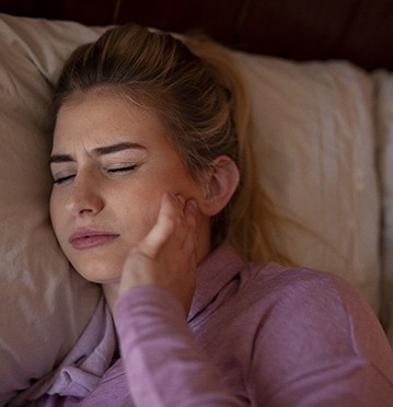 Young woman in bed with jaw pain from bruxism and TMJ disorder
