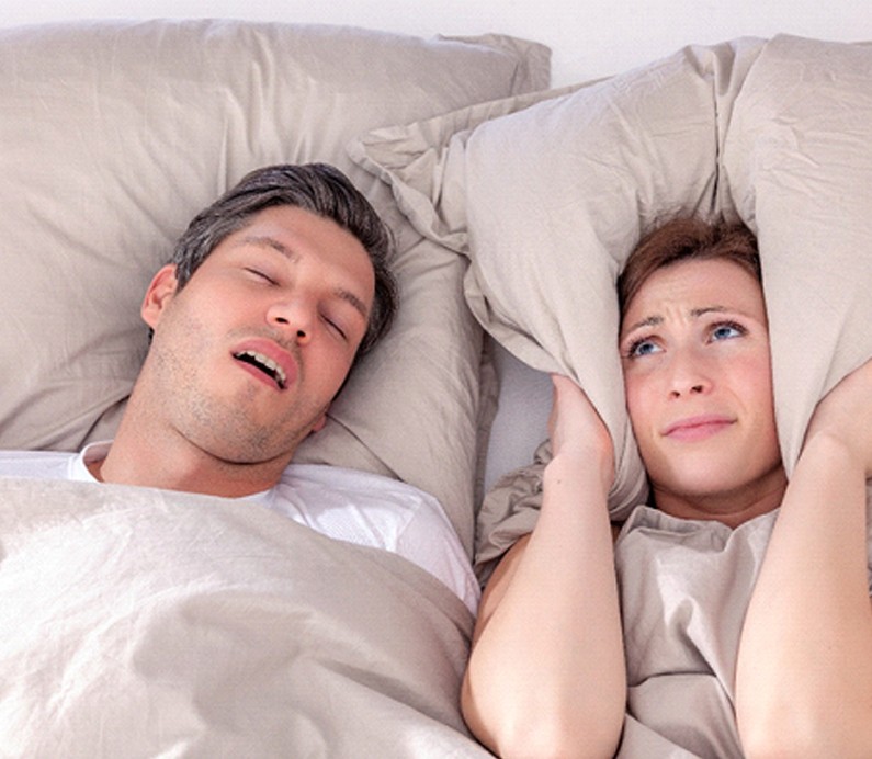 Woman covering ears next to snoring man with sleep apnea in Albuquerque New Mexico