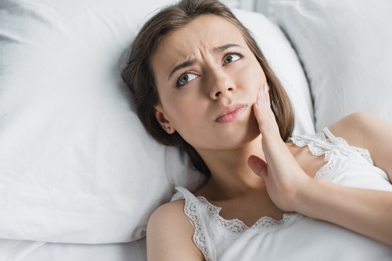 person lying in bed and holding their jaw in pain