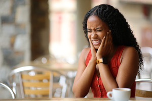 Woman in a restaurant with jaw pain from TMJ disorder