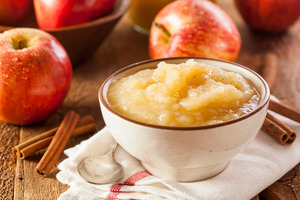 A bowl of applesauce surrounded by apples